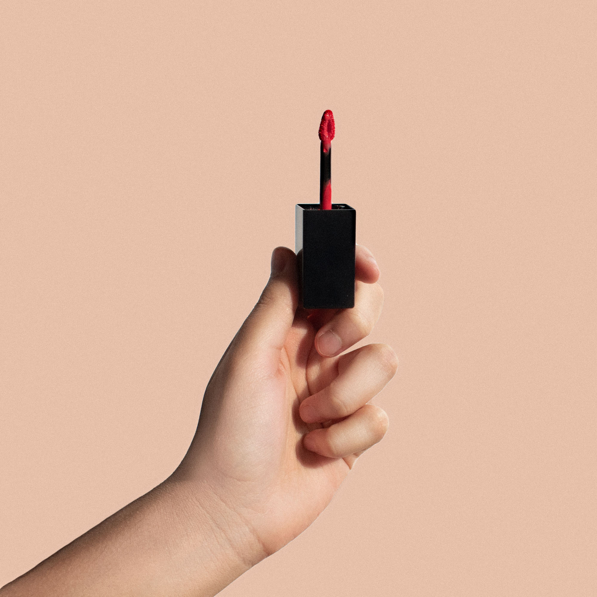 Hand holding Erinelle Beauty lip glow color reviver balm with red applicator against beige background
