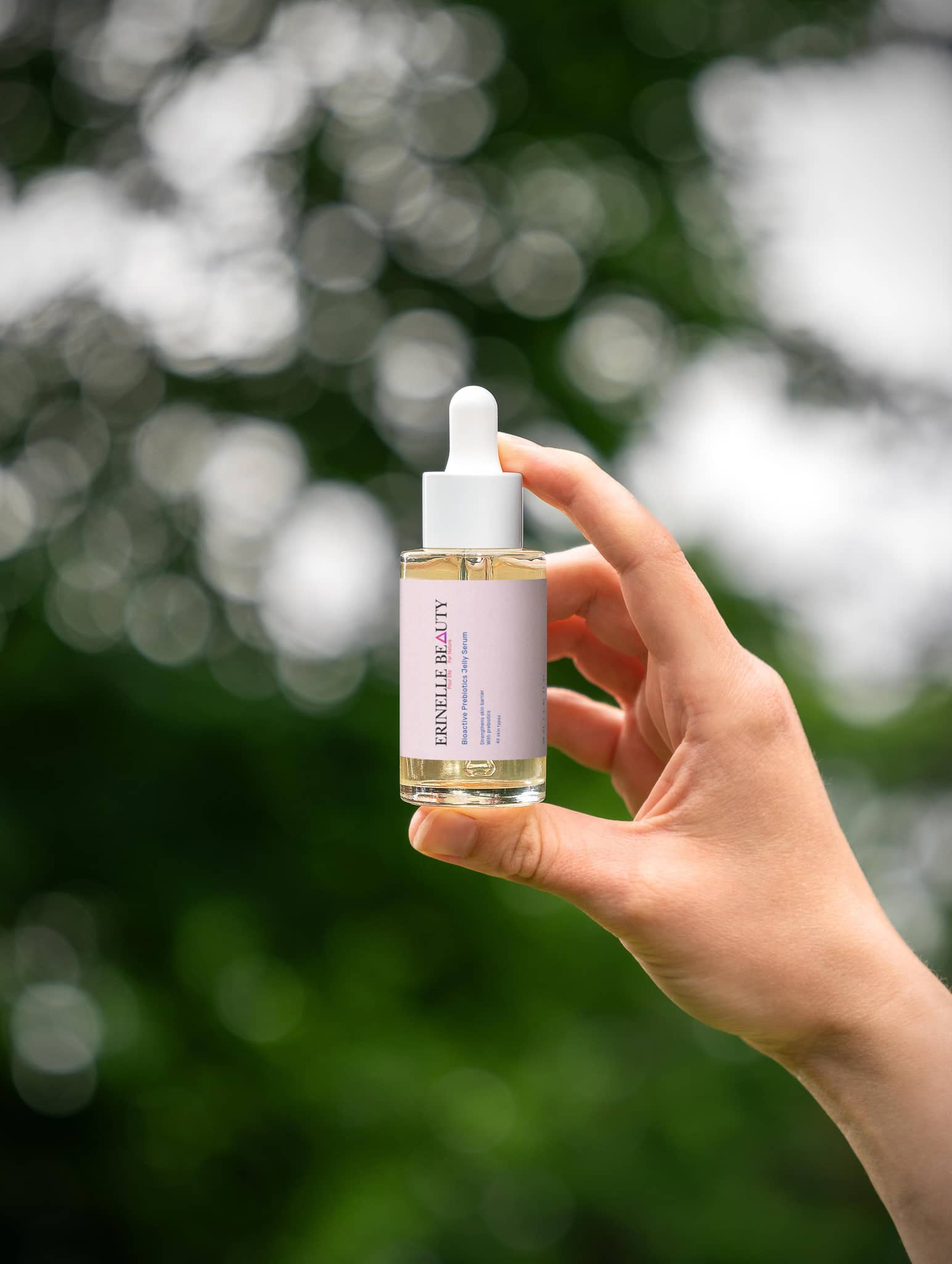 Erinelle Beauty hydrating serum with prebiotics held in hand against blurred green background