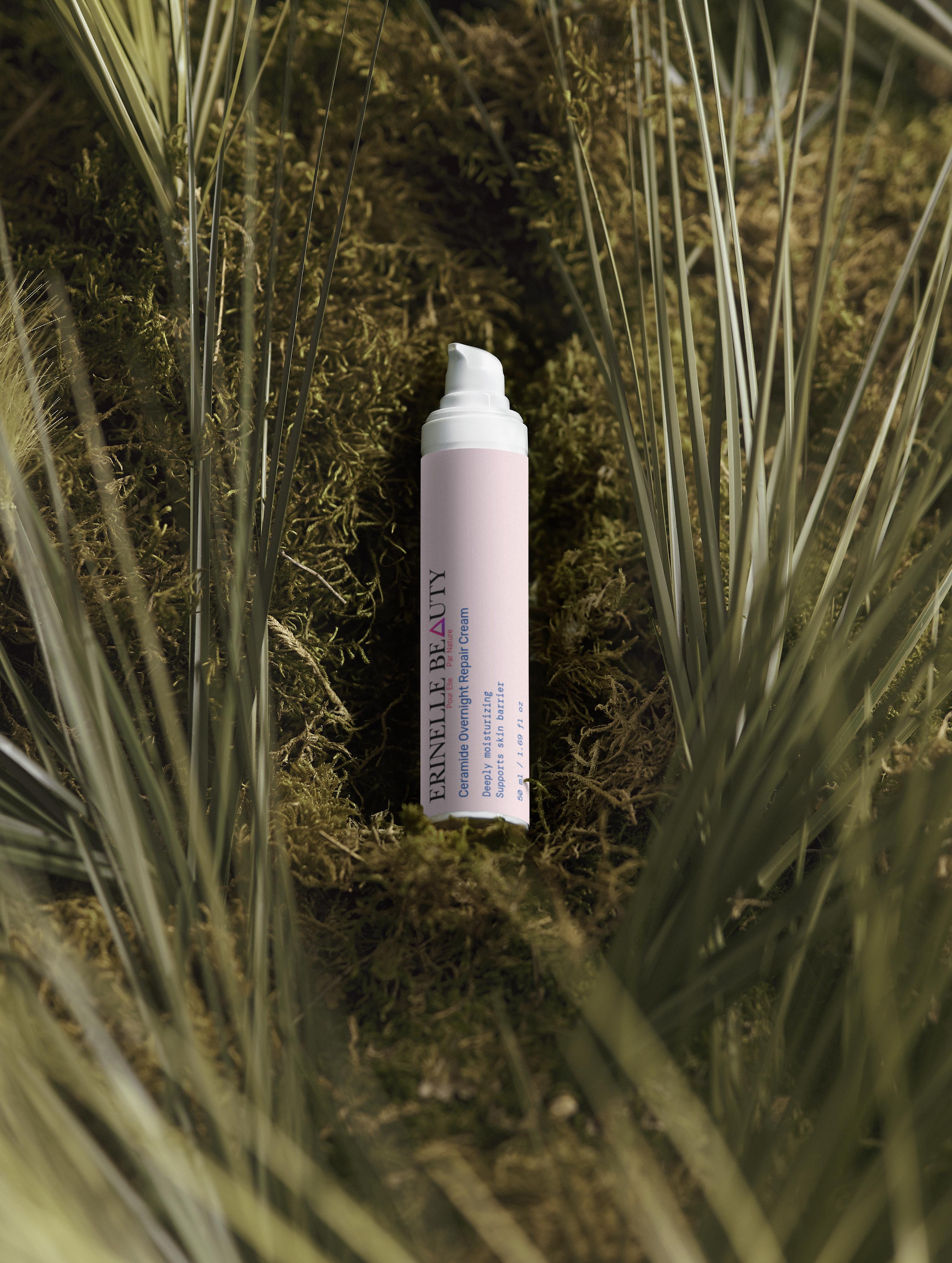 Erinelle Beauty ceramide overnight repair cream bottle placed on green moss surrounded by grass blades